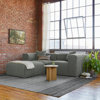 Gray textured sectional sofa with a cozy throw, accent pillows, and a striped gray area rug in a modern industrial setting.