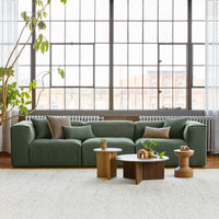 Green textured sofa with neutral accent pillows, paired with light wood and round coffee tables, in a bright room.