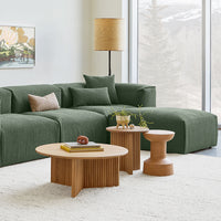 Green textured sectional sofa with beige accent pillows, complemented by wooden coffee tables in natural tones.