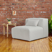 Light gray textured lounge chair on wooden floor, contrasted by warm, rustic red brick wall.
