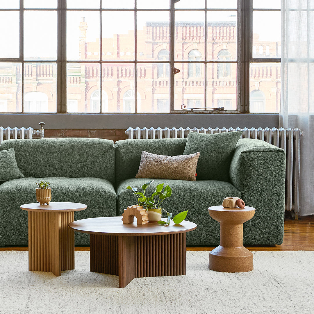 Green textured couch with neutral accent pillows, paired with wooden tables in natural tones and a light area rug.