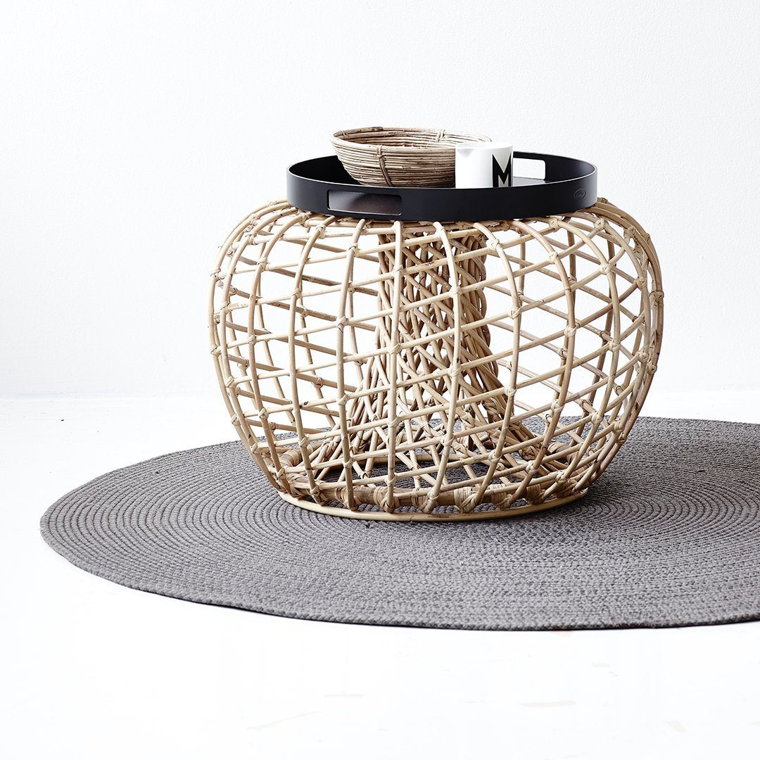 Woven rattan basket in natural beige with a sleek black rim, set atop a textured gray round rug.