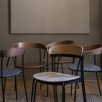 Set of modern chairs with natural wood finishes and dark metal frames on a textured floor, against a neutral backdrop.