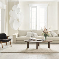 Neutral beige sofa with white accents, light wooden floor, and soft cream rug, complemented by floral decor.