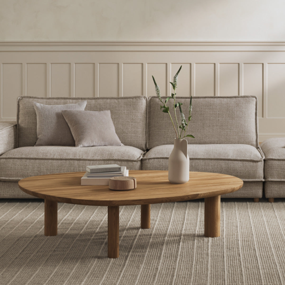 Natural oak coffee table on a light textured rug, surrounded by soft beige and gray upholstered sofas and pillows.