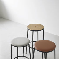 Three stools featuring gray, tan, and brown circular seats with black metal legs against a minimalist backdrop.