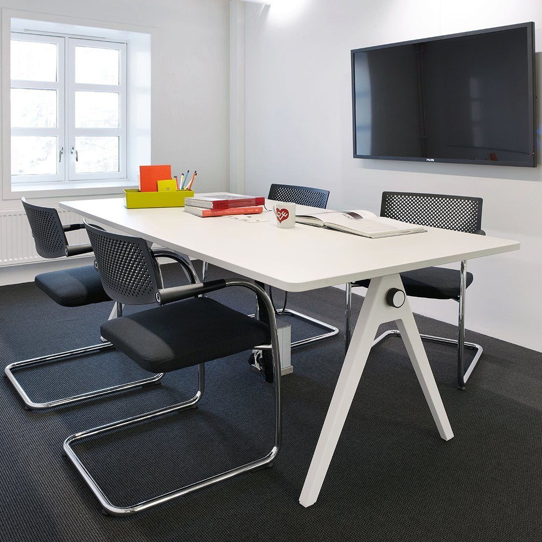 Modern white table with black mesh chairs and colorful stationery elements in a sleek, minimalist office setting.