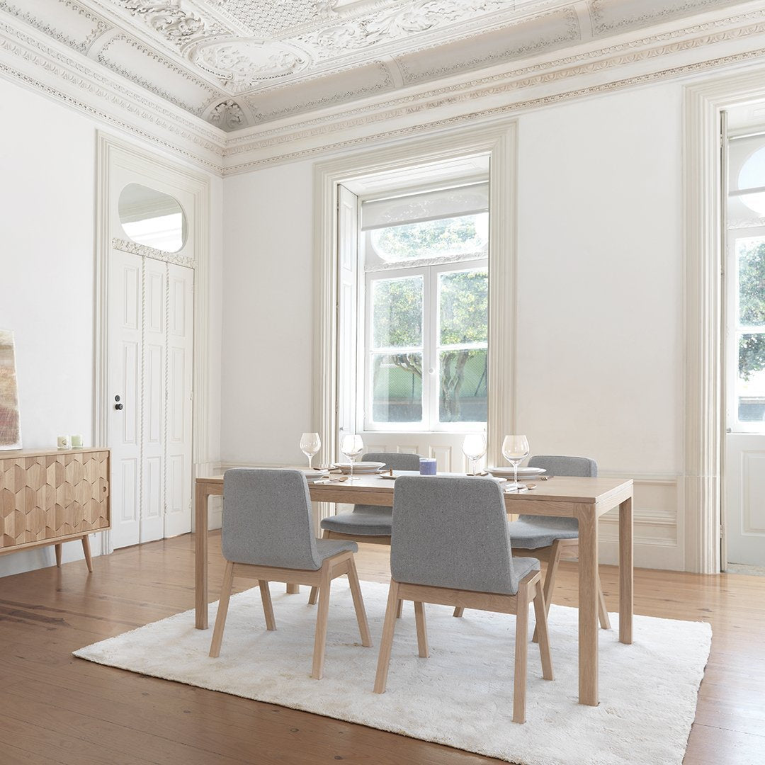 Light wood dining table with grey chairs, soft textured rug, and neutral wall colors, creating a serene and modern ambiance.