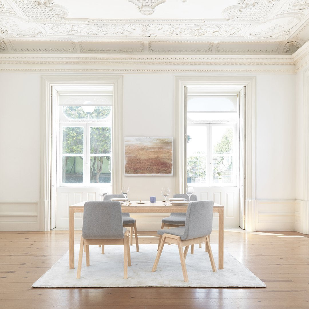 "Modern dining room with light gray chairs, natural wood table, and neutral-toned abstract wall art on white backdrop."