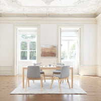 "Modern dining room with light gray chairs, natural wood table, and neutral-toned abstract wall art on white backdrop."