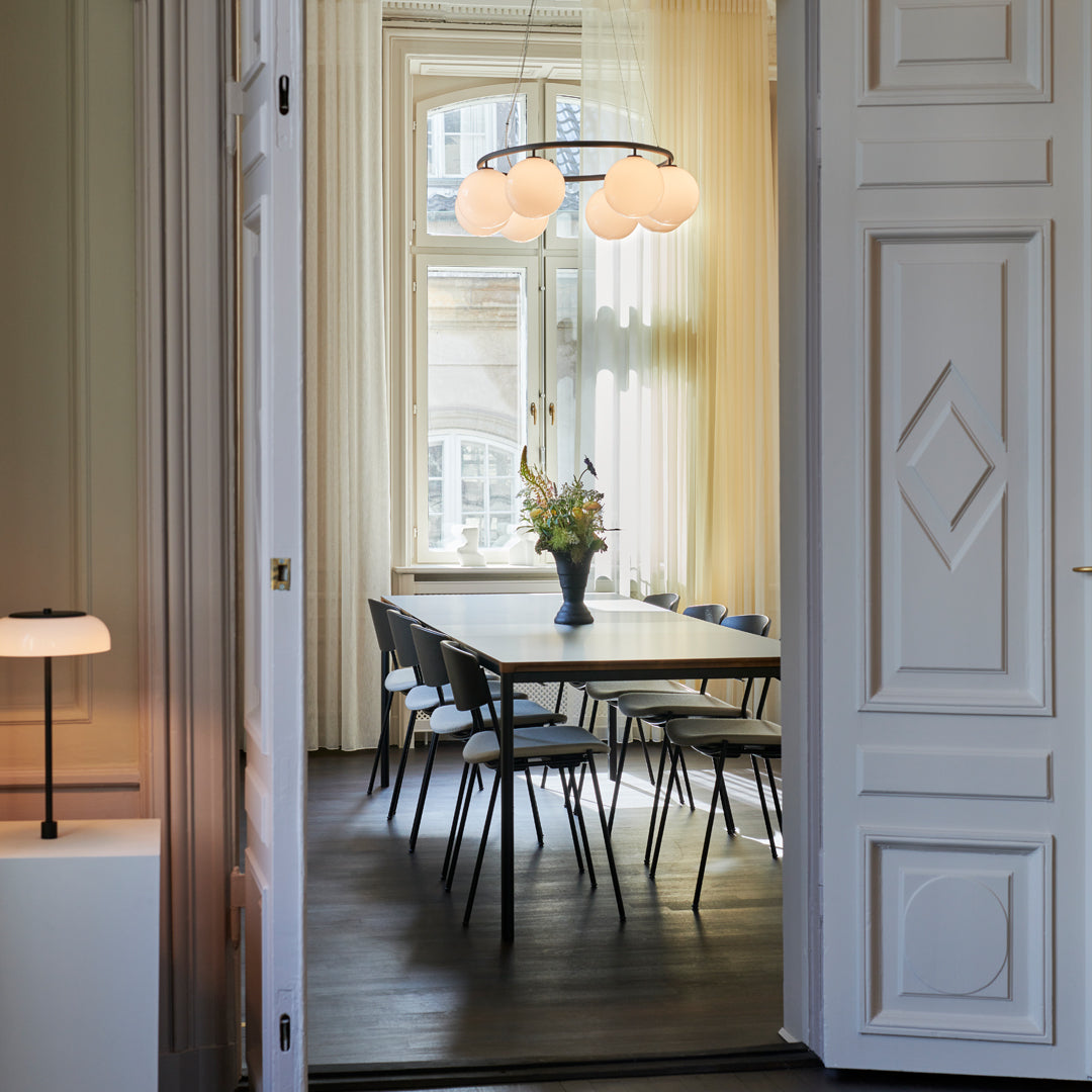 Elegant interior featuring soft cream curtains, a sleek black dining table, and patterned vase with fresh flowers.