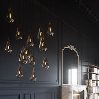Elegant pendant lights with clear glass droplets and warm gold accents against a dark wall backdrop.