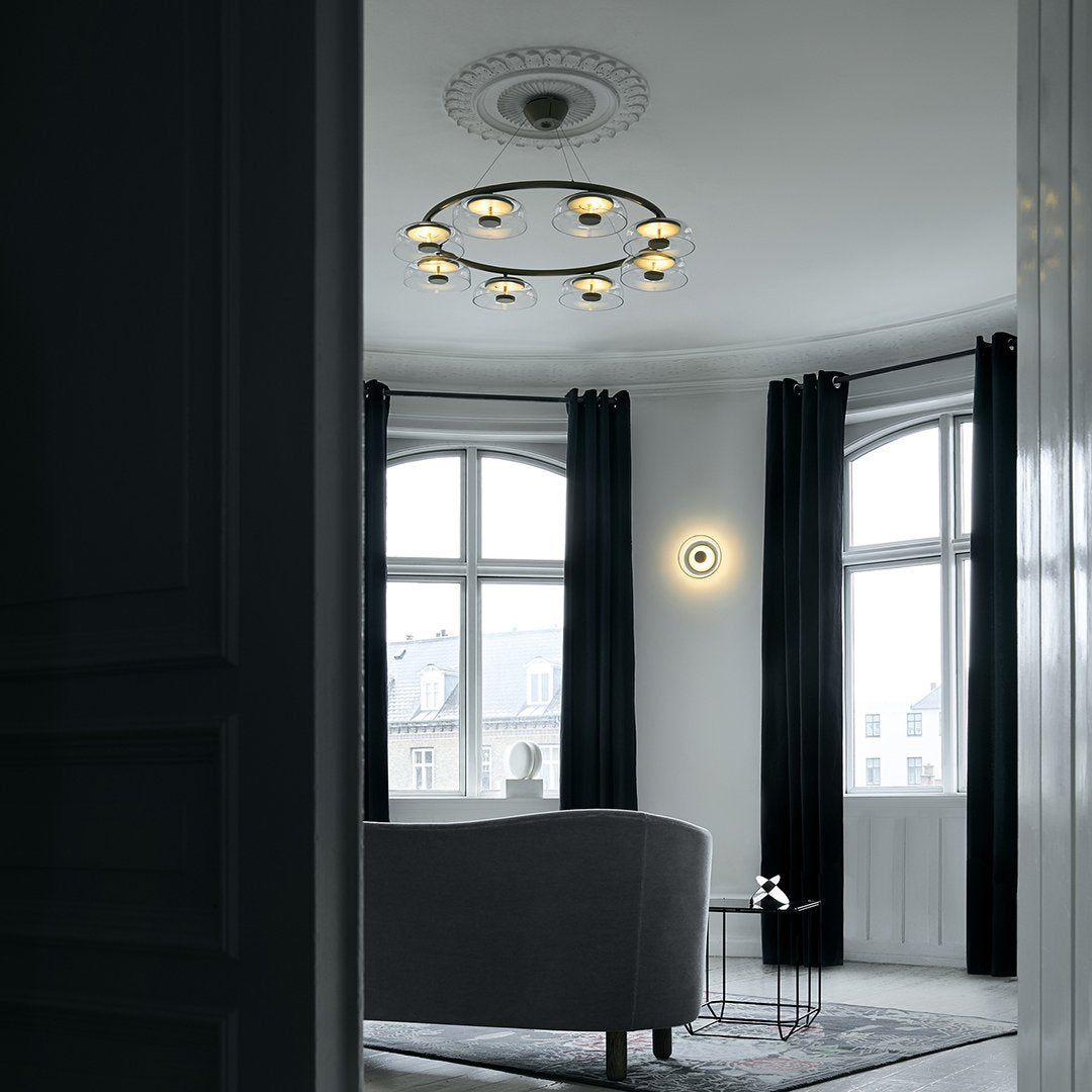 Modern gray sofa with black curtains and a minimalist light fixture in a light-filled, neutral-toned room.