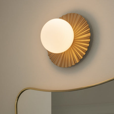 Gold wall sconce with a ribbed circular base and a round white globe light, perfect for modern decor.