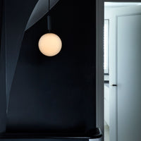 Minimalist pendant light with a soft white orb against a deep black wall, creating a modern contrast.