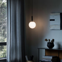 "Glossy white pendant light against dark gray curtains and a textured wall with abstract patterns."