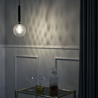 Orb-shaped pendant light casting soft, textured shadows on a light gray wall, accented by deep blue curtains.