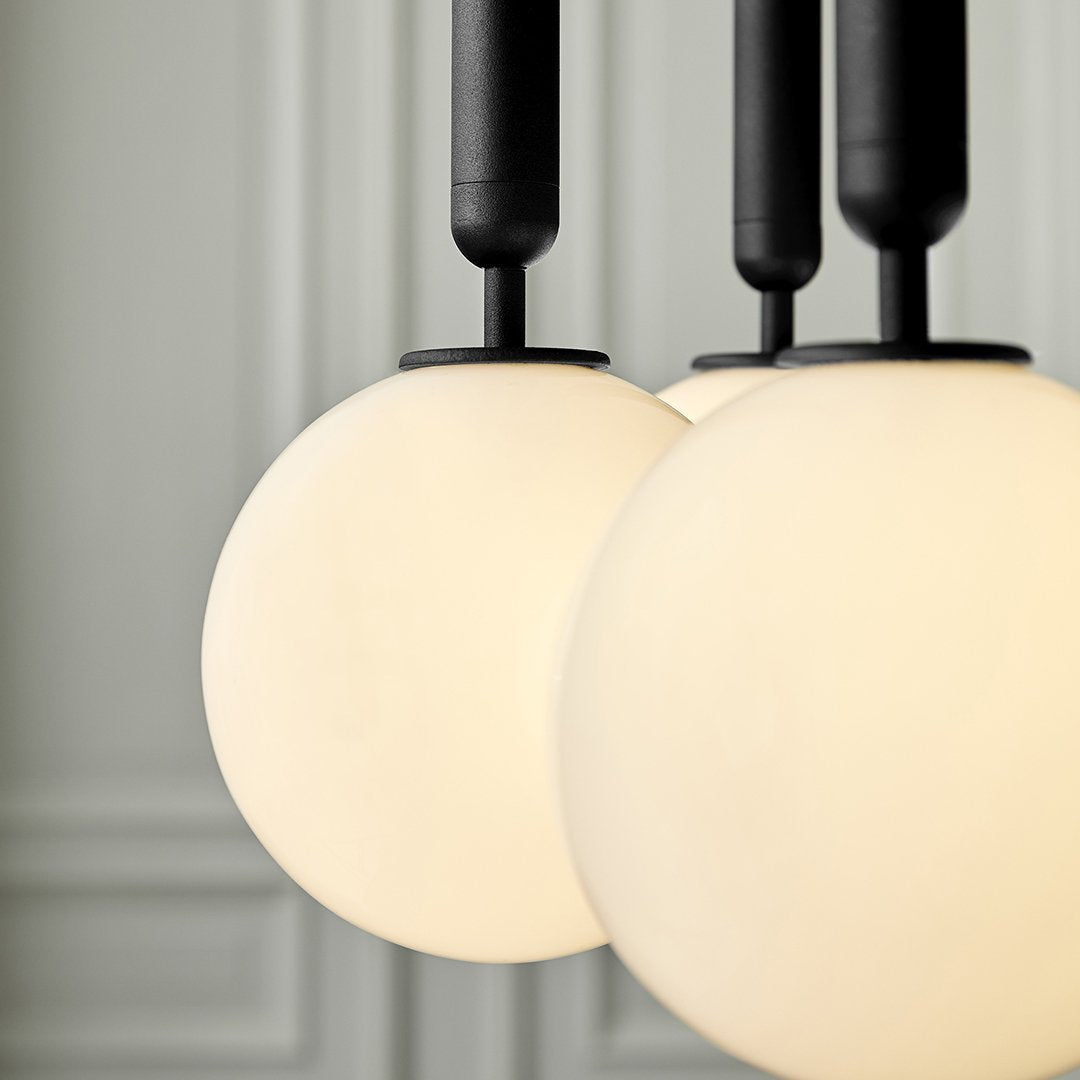 Three round, frosted white glass pendant lights with sleek black accents against a subtle textured backdrop.