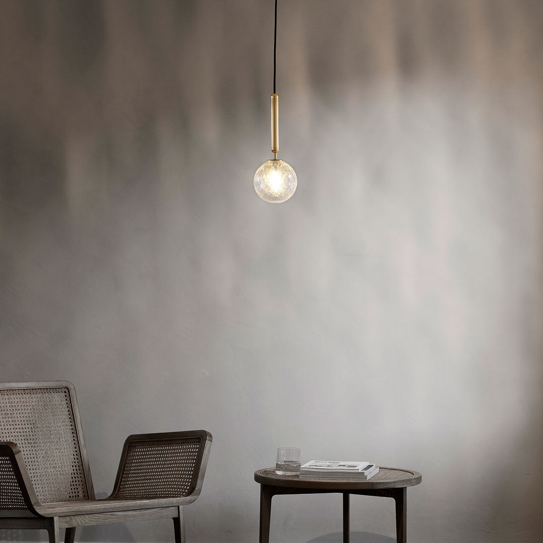 Modern pendant light with a clear glass orb and sleek brass accents, set against a soft gray wall.