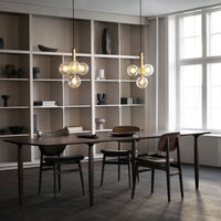 Modern dining room featuring warm wood tones, black seating, and stylish glass pendant lights against a neutral backdrop.