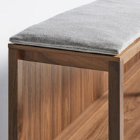 Gray upholstered bench cushion atop warm walnut wood frame with rich grain pattern. Perfect for modern interiors.