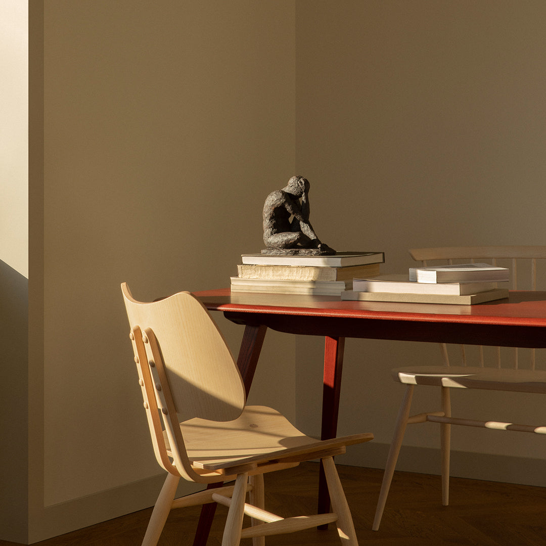 Light wooden chair and red table with neutral tones, books stacked in white and cream, creating a warm, minimalist look.