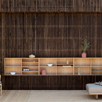Light wood shelving unit with white bowls and pink vases against a dark, patterned wooden backdrop. Elegant and modern design.