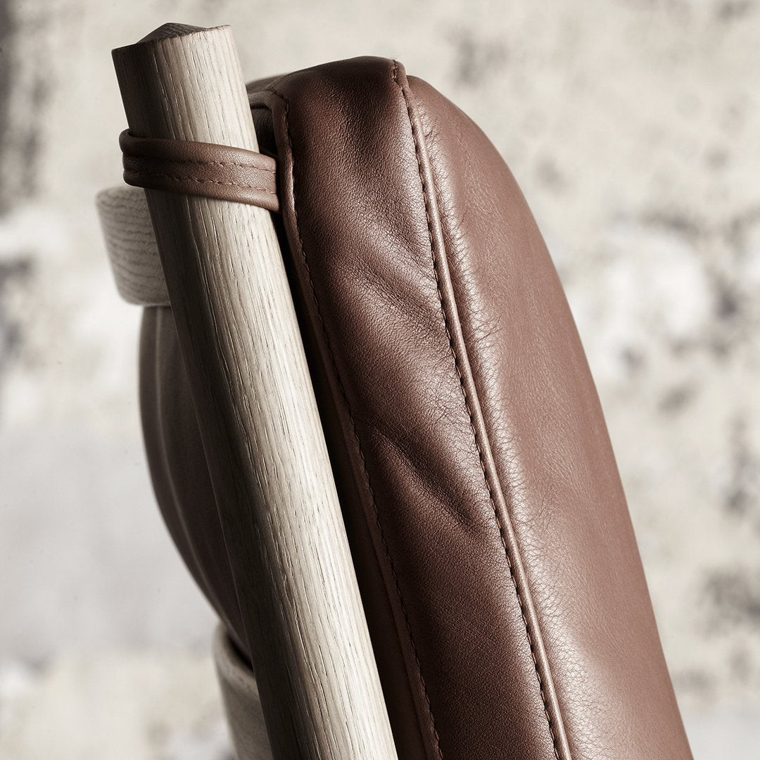 Brown leather cushion with a smooth texture, paired with a light wooden frame, showcasing a minimalist design.