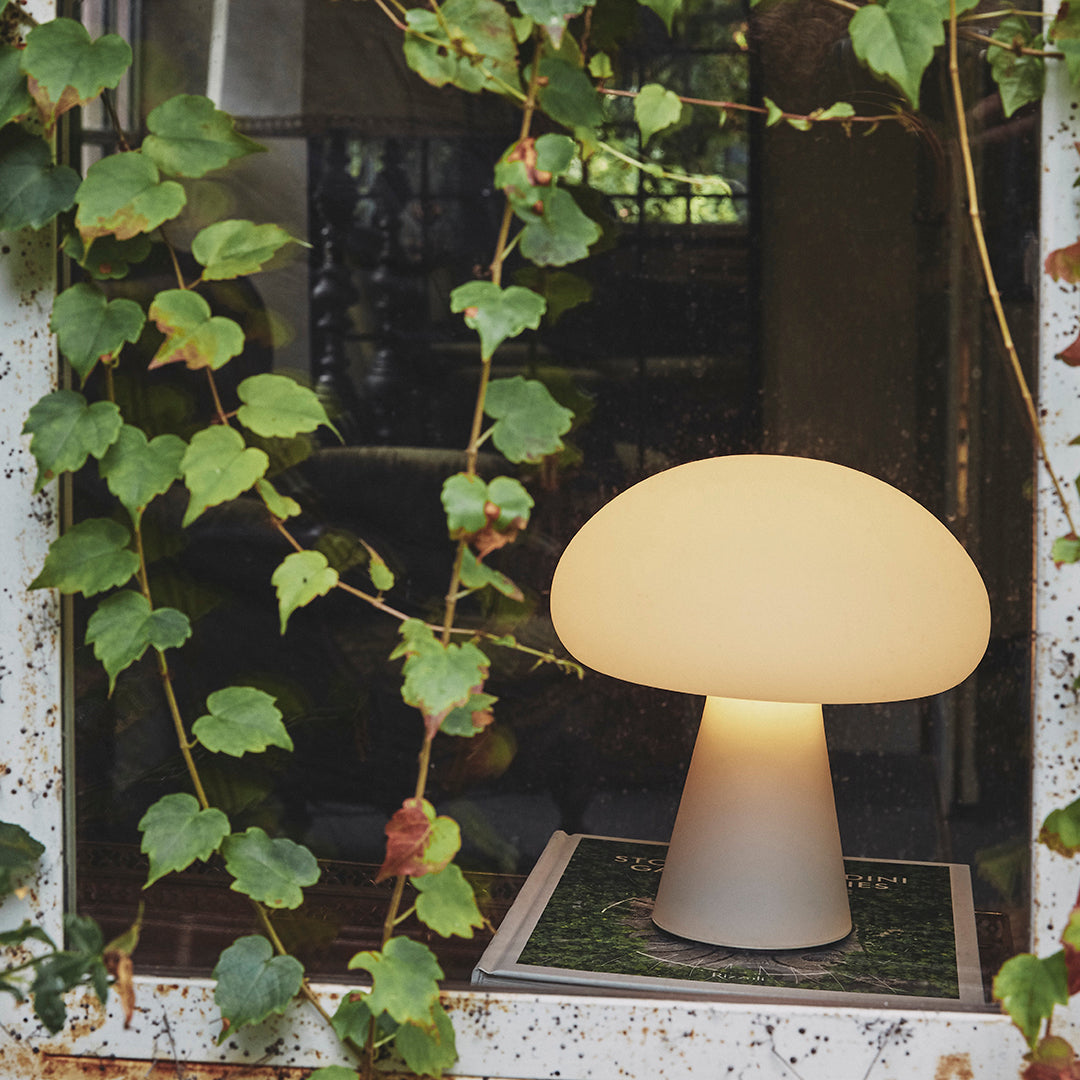 Soft white mushroom-shaped lamp surrounded by vibrant green ivy, set against a rustic window frame.