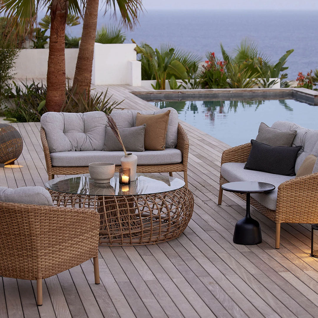 Cozy light gray seating with taupe cushions, accompanied by a woven rattan table, set against a tropical backdrop.