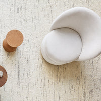 Light beige textured chair on a cream rug with subtle gray patterns, complemented by brown and cork accent tables.