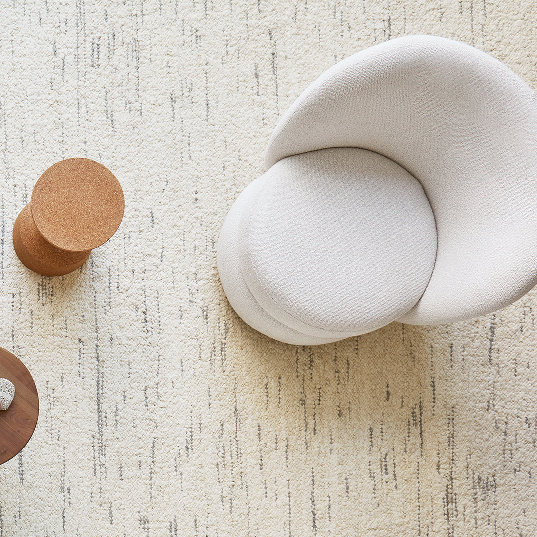 Minimalist white chair on textured beige rug with subtle gray patterns and a round cork side table.