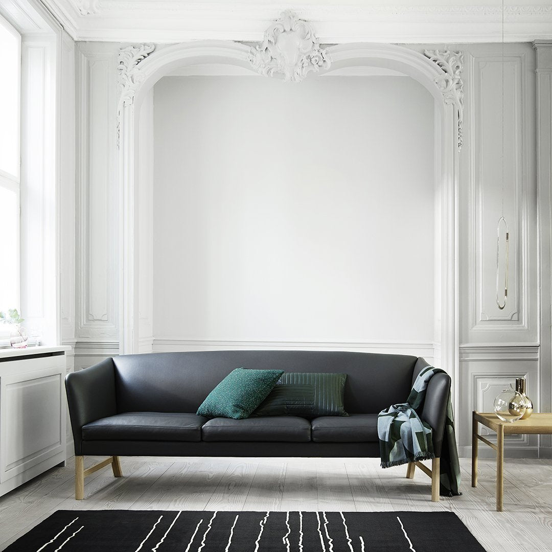 Black sofa with green cushions, paired with a patterned black rug featuring white lines, set in a sophisticated room.