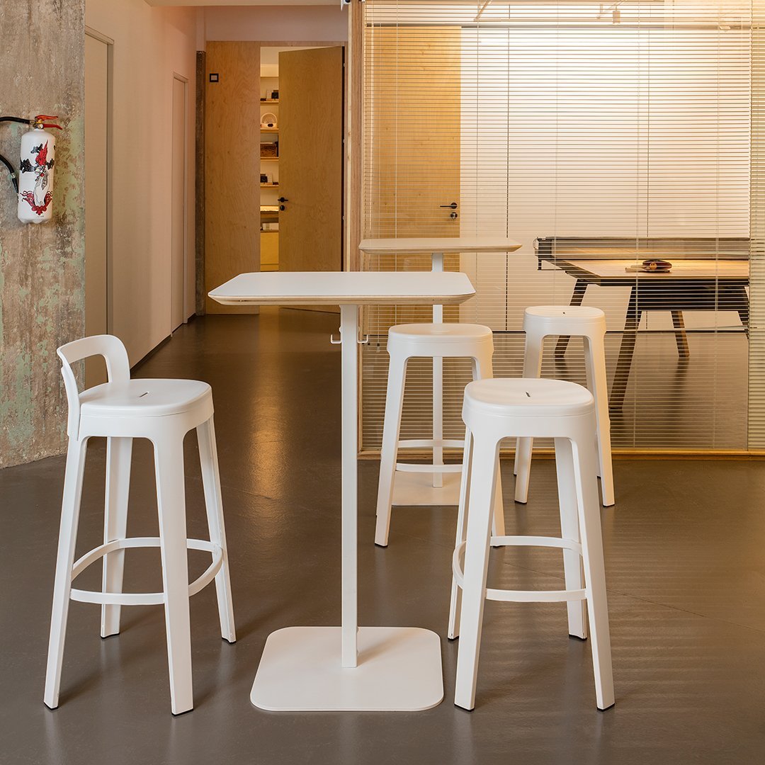 White bar stools and table in a modern interior with gray flooring and wooden accents, featuring a clean, minimalist design.