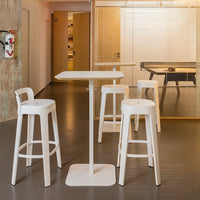 White bar stools and table in a modern interior with gray flooring and wooden accents, featuring a clean, minimalist design.