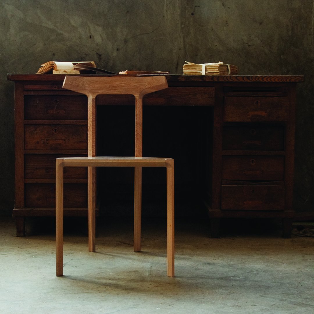 Natural wood chair with a minimalist design, showcasing light brown hues against a textured gray background.