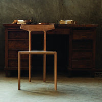 Natural wood chair with a minimalist design, showcasing light brown hues against a textured gray background.
