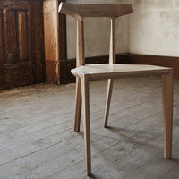 Light wood chair with a natural finish, featuring sleek lines and minimalistic design against a rustic background.