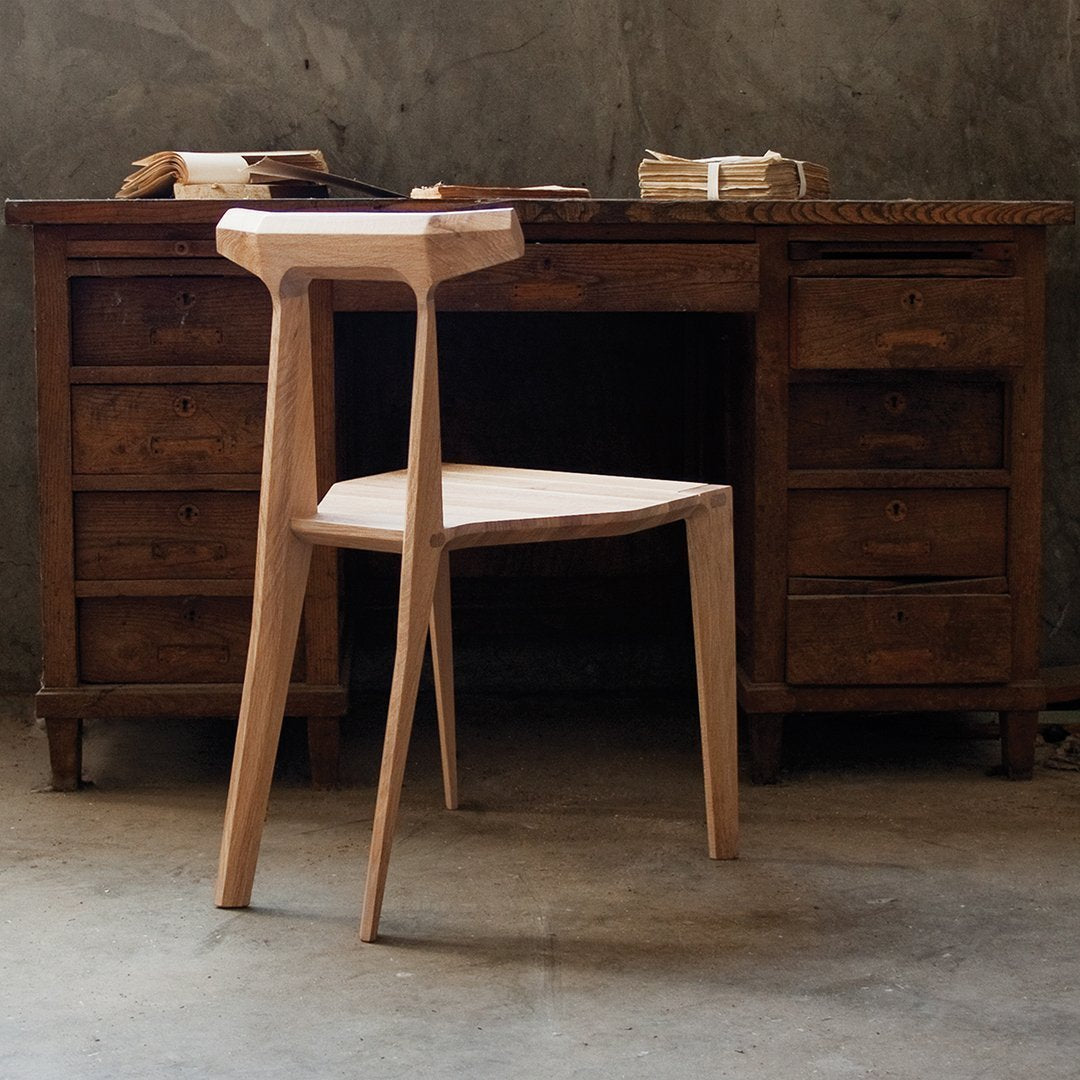 Light wood stool with a sleek, minimalist design, featuring natural grain and smooth finish against a rustic wooden desk.