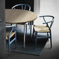 Light wood round table with blue chairs featuring woven seat patterns, set on a textured gray rug.