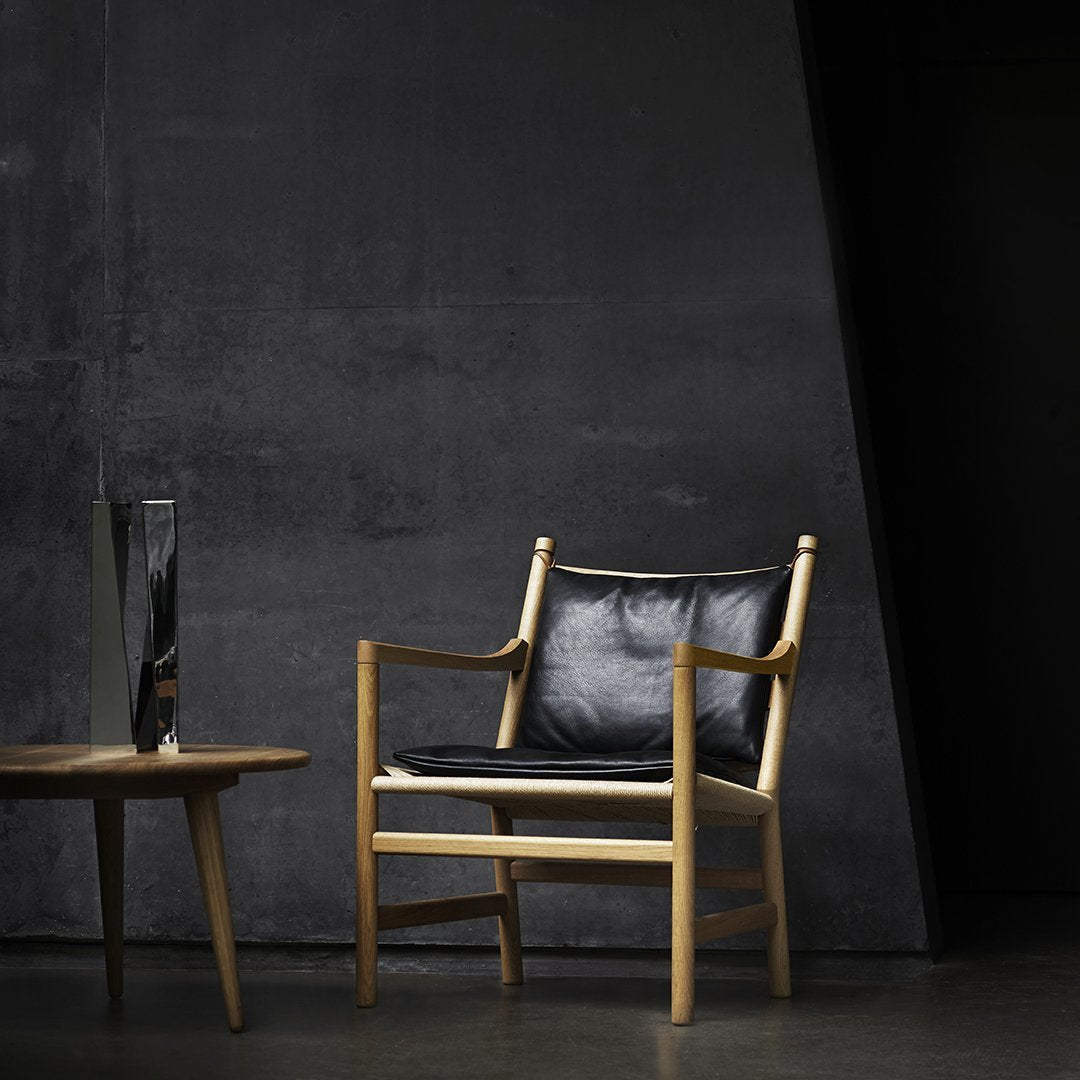Modern black leather chair with light wood frame against a dark, textured background. Sleek and minimalistic design.