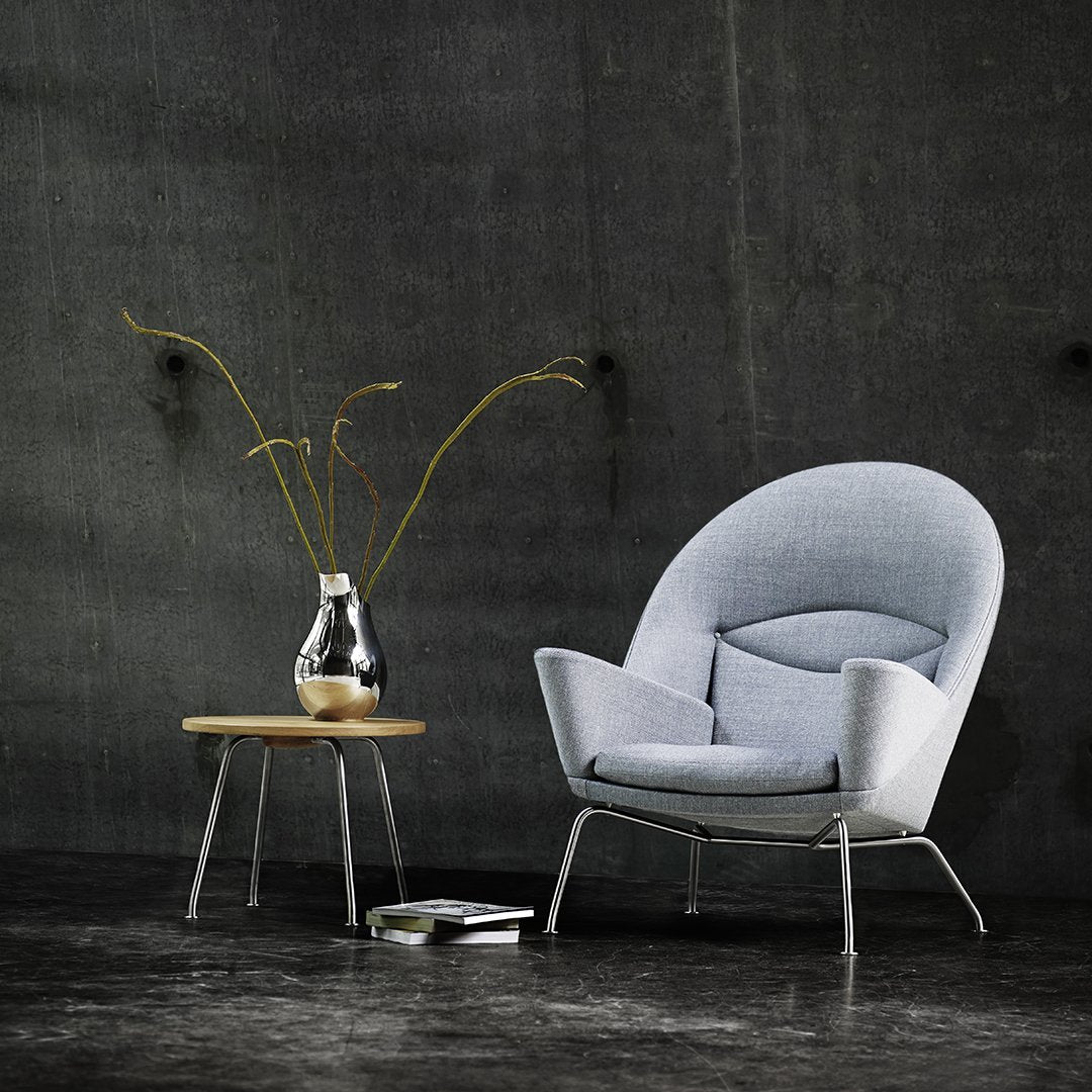 Light gray upholstered chair with a smooth texture, paired with a natural wood table, set against a dark, modern backdrop.