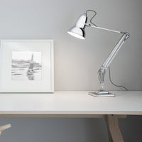"Silver desk lamp with a sleek, minimalist design, paired with a monochrome art print on a light wood table."