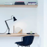 Black desk lamp, blue patterned chair, neutral shelf, and colorful books create a modern workspace aesthetic.