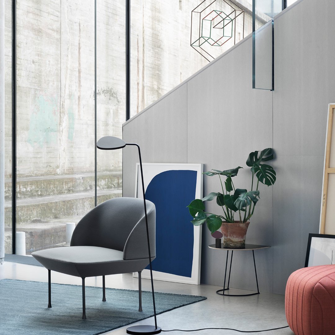 "Modern gray chair with black accents, geometric wall art in blue, and a green plant in a stylish interior setting."