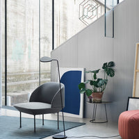 "Modern gray chair with black accents, geometric wall art in blue, and a green plant in a stylish interior setting."