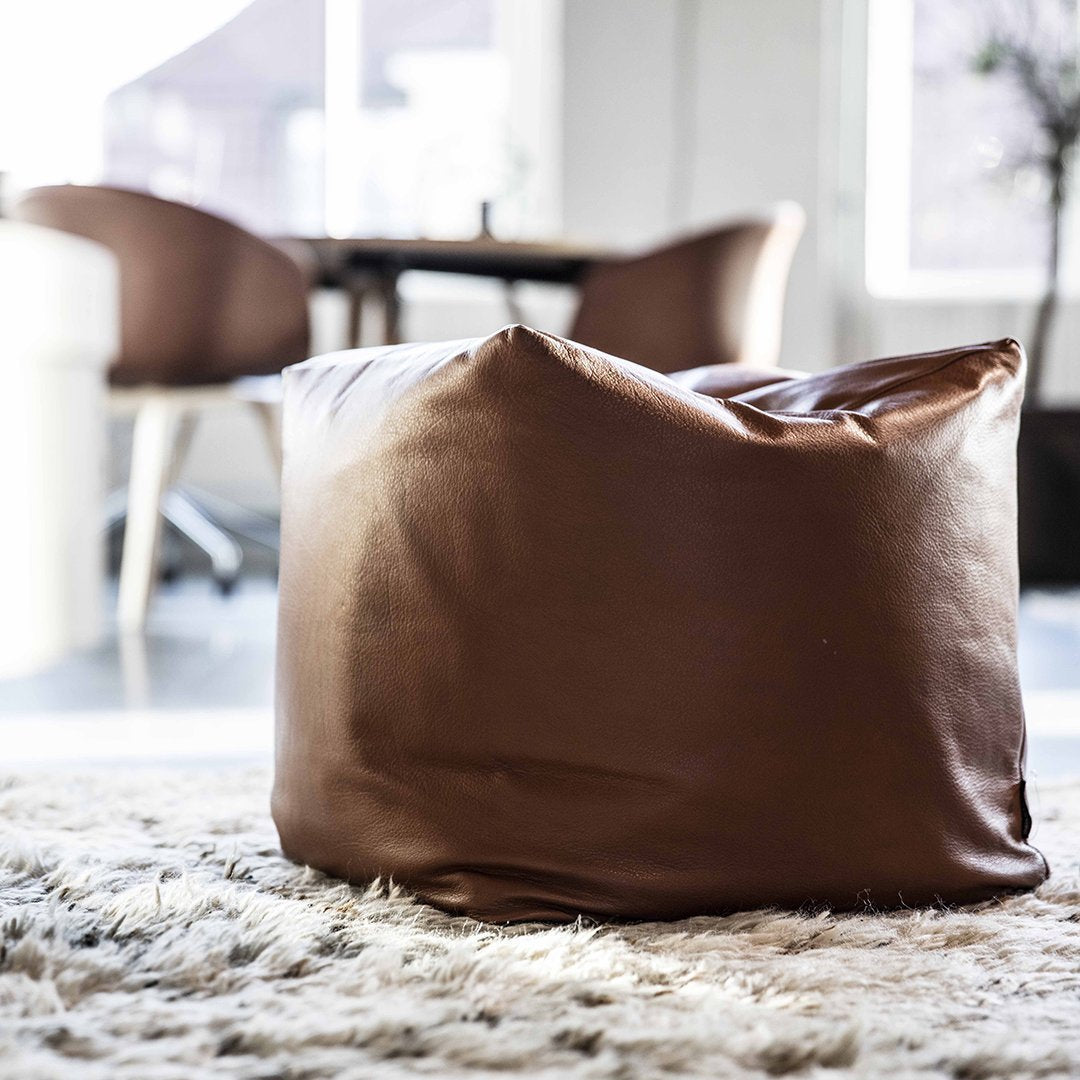 Brown faux leather bean bag in a minimalist interior setting, featuring smooth, solid color and contemporary design.