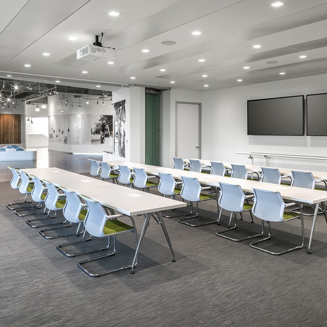 Modern conference room featuring light blue chairs and a sleek, minimalist table with green accents on gray carpeting.