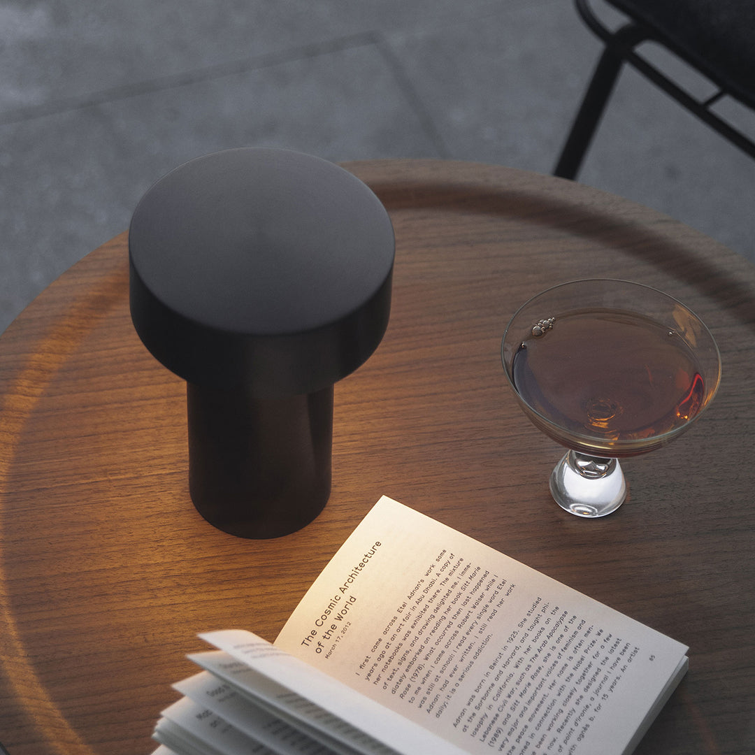 Black cylindrical lamp on a wooden table, with a clear glass, highlighting modern minimalism and elegant contrasts.