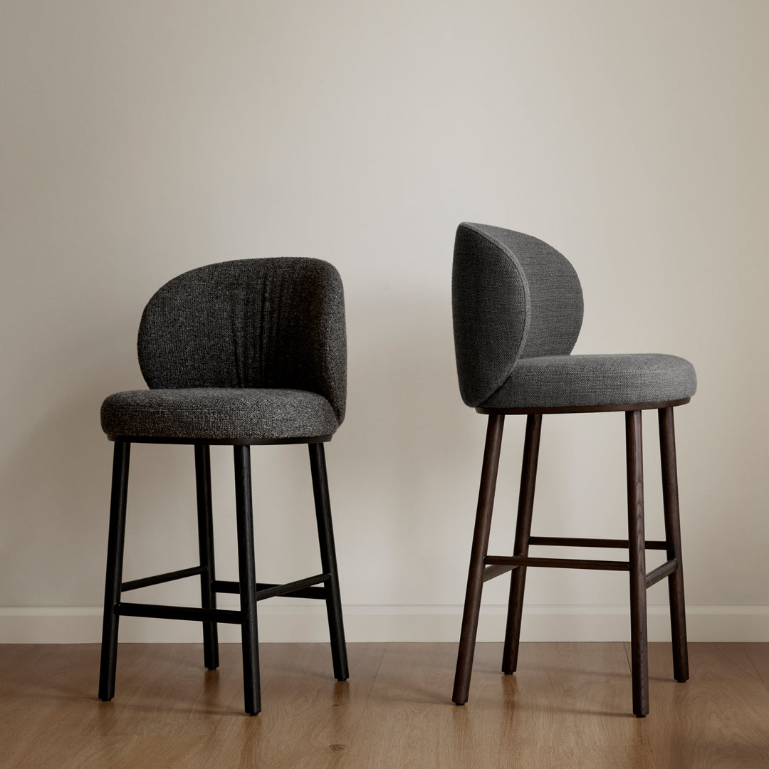 Two sleek bar stools in textured charcoal gray, featuring curved backs and contrasting black and dark wood legs.